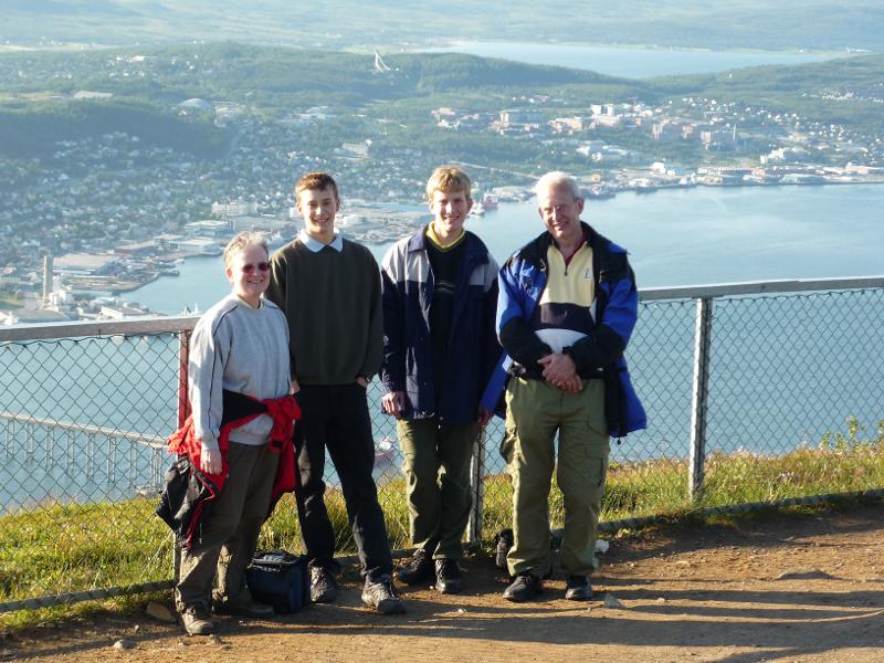 Familiefoto på en høyde med en by i bakgrunnen. To brødre med sine foreldre. 